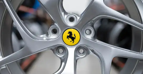 Ferrari 812 alloy wheel with yellow centre badge in warehouse with other wheels blurred in background.